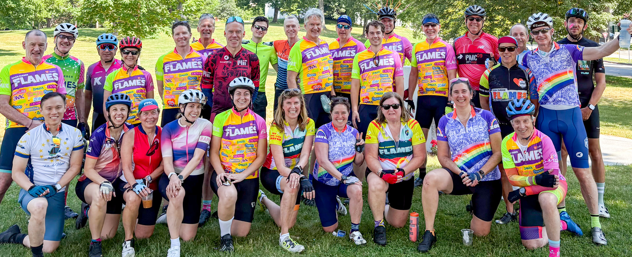 About thirty-five Dana-Farber FLAMES riders in team jerseys posed on a lawn in two rows after a training ride